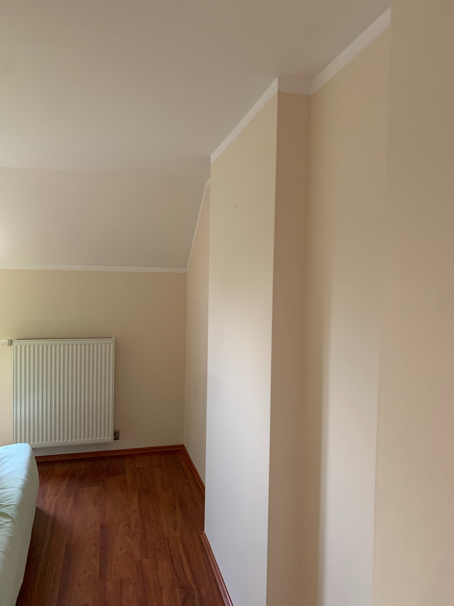 Jasne wnętrze po odświeżeniu: kremowe ściany z białym pasem pod sufitem, drewniana podłoga, grzejnik. Widok z perspektywy narożnika pokoju.