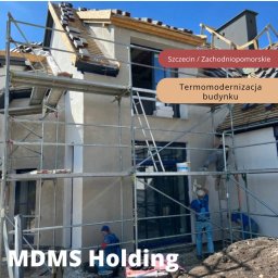 MDMS HOLDING Spółka z o.o. - Budynek w trakcie termomodernizacji, widoczne rusztowania i pracownicy wykonujący prace elewacyjne oraz układanie dachówki.