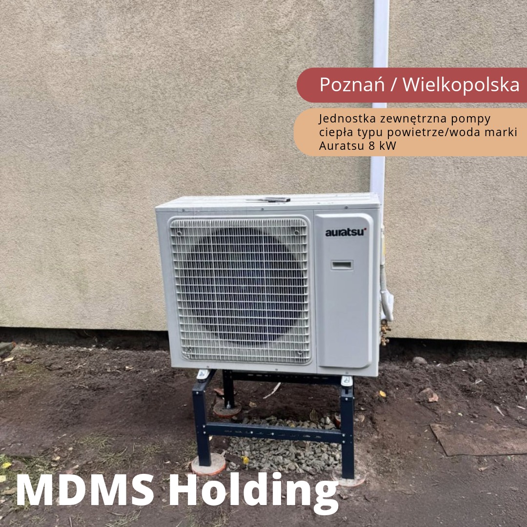 Zewnętrzna jednostka urządzenia grzewczego marki Auratsu, model powietrze/woda 8kW, zamontowana na czarnej, metalowej konstrukcji wsporczej przy ścianie budynku.