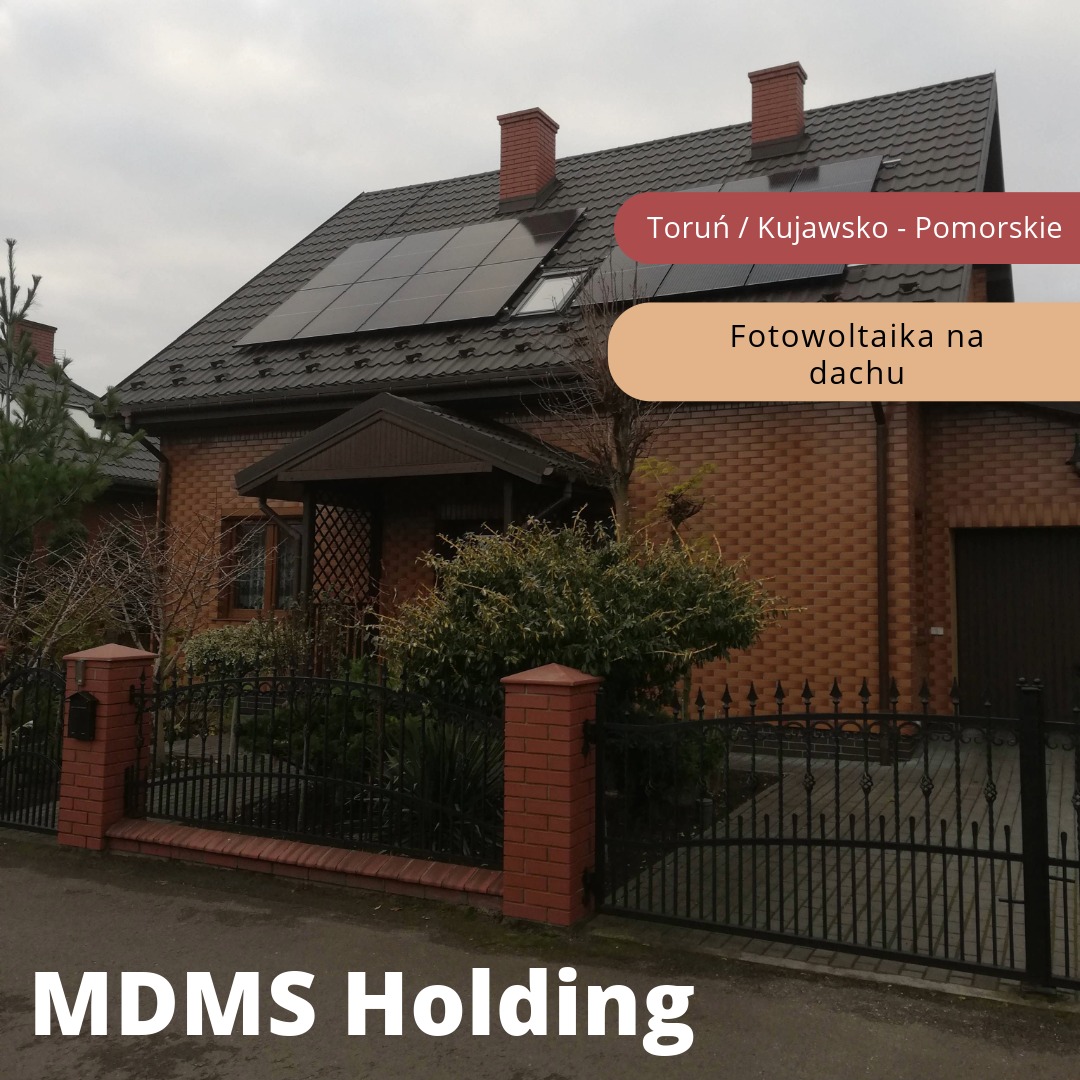 Dom jednorodzinny z brązowej cegły z panelami słonecznymi na dachu, widoczne ogrodzenie z ceglanymi słupkami i czarnym metalem.