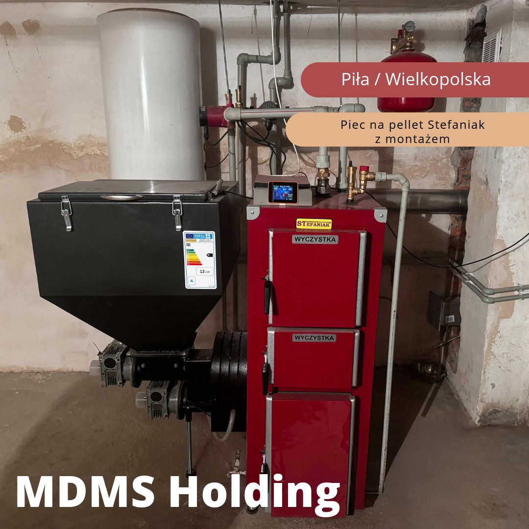 Zainstalowany piec na pellet marki Stefaniak z zasobnikiem, widoczne przyłącza hydrauliczne, sterownik i etykieta energetyczna, tło stanowi ściana z widocznymi śladami użytkowania.