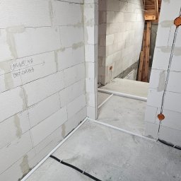 Mateusz Mrugała - Wnętrze w trakcie budowy z instalacją elektryczną w ścianach z betonu komórkowego. Widoczne puszki elektryczne i rury osłonowe. Na ścianie notatki o rozmieszczeniu umywalki.