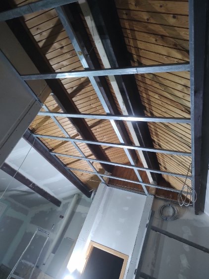 Drewniany sufit z widoczną konstrukcją metalową pod płytę karton gips, częściowo wykończone ściany gładzią.