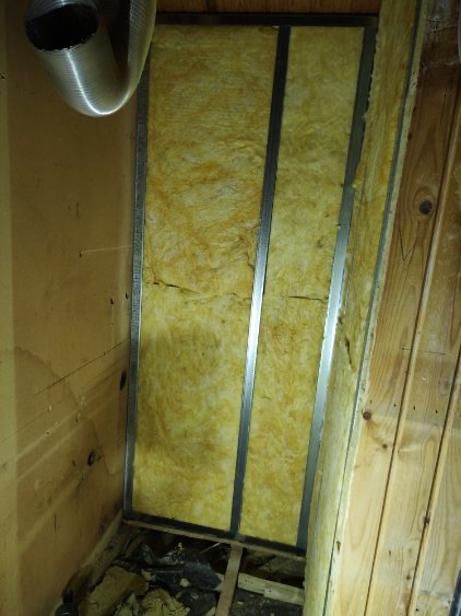 Izolacja termiczna ściany wełną mineralną w metalowym stelażu, widoczny fragment wentylacji i drewniane elementy konstrukcyjne.