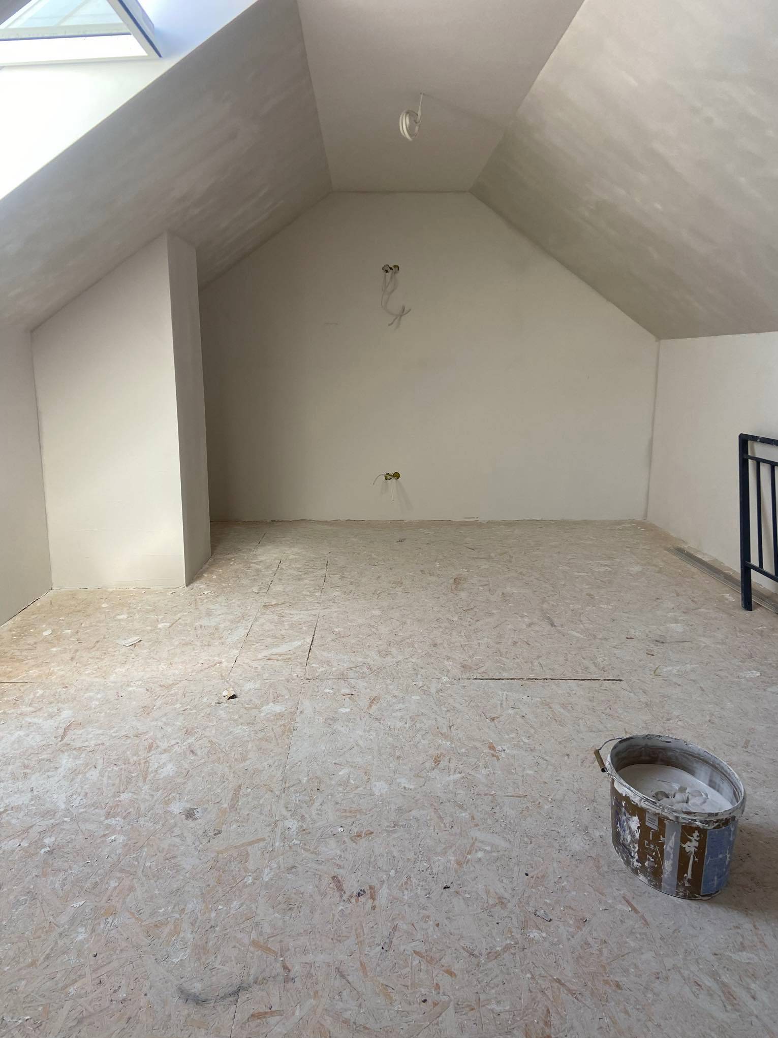 Poddasze po nałożeniu gładzi, widoczny sufit z oknem dachowym, ściany pokryte świeżą gładzią, na podłodze płyta OSB z resztkami gładzi, w rogu wiadro z gładzią.
