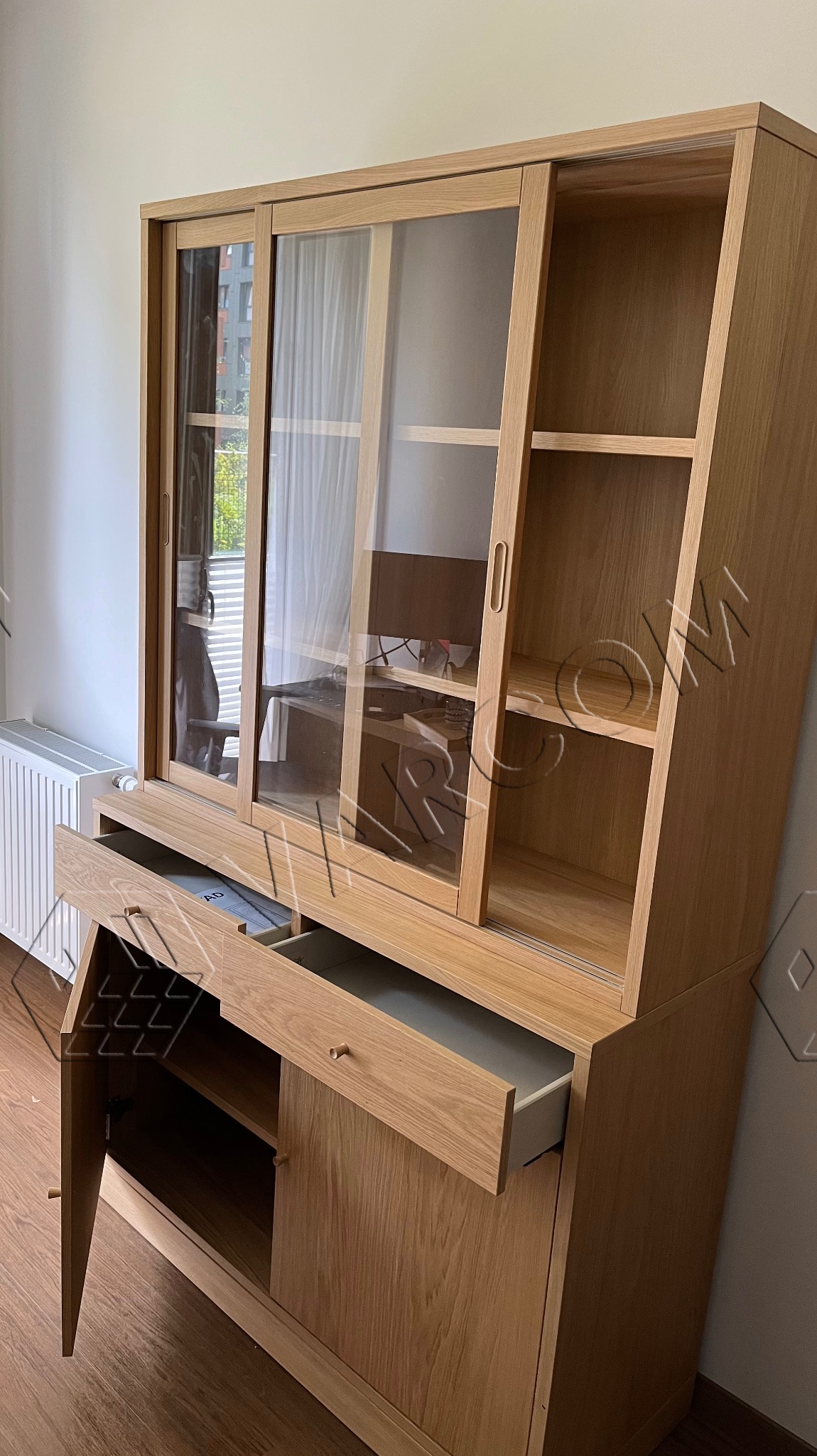 Jasna, drewniana witryna z przesuwanymi szklanymi drzwiami, otwartymi szufladami i szafką, widok na wnętrze z biurkiem i komputerem, minimalistyczny design.