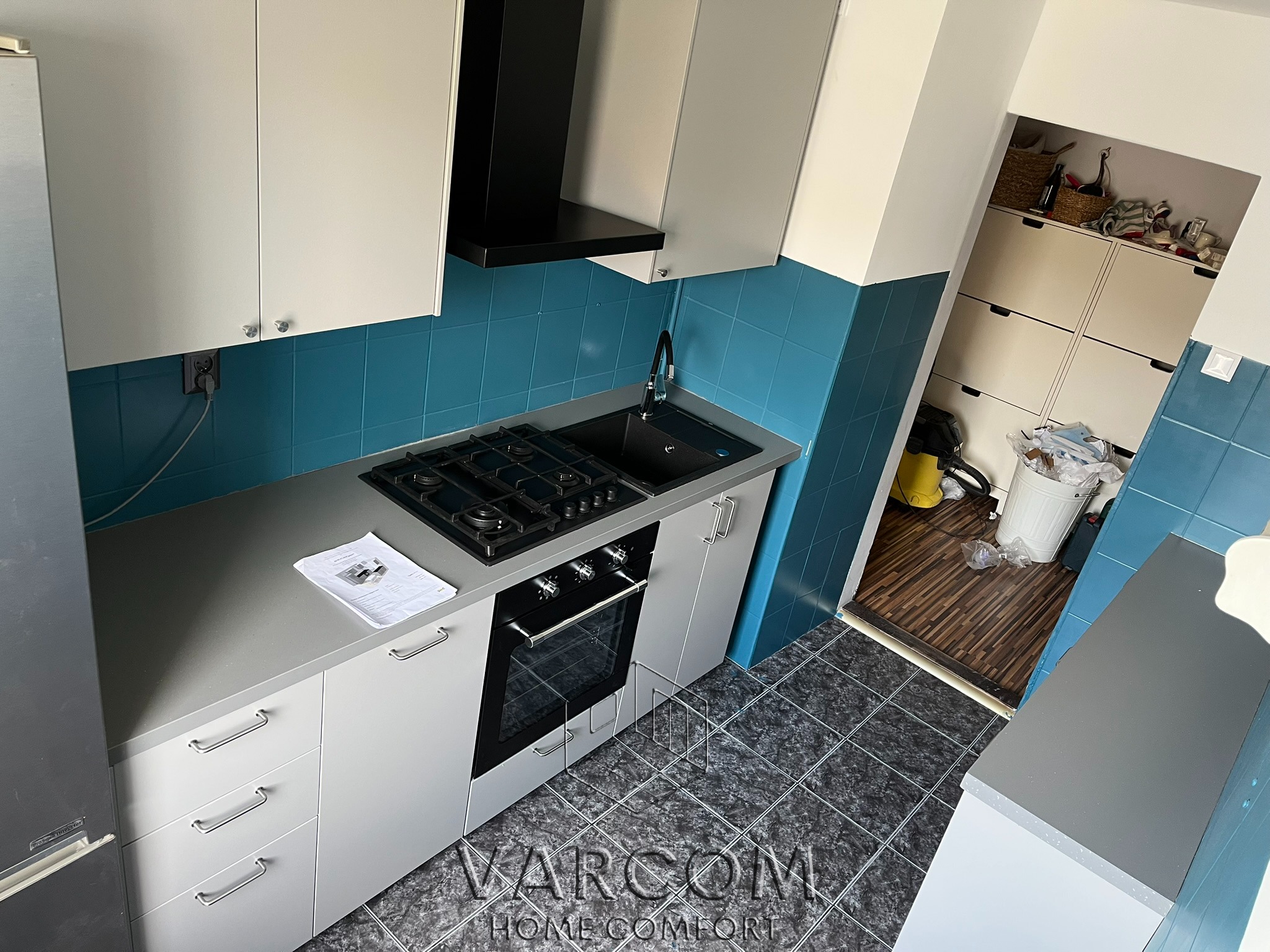 Nowoczesna kuchnia z białymi szafkami, turkusowymi płytkami i szarym blatem. Widok z góry ukazuje detale wykończenia i układ funkcjonalny.