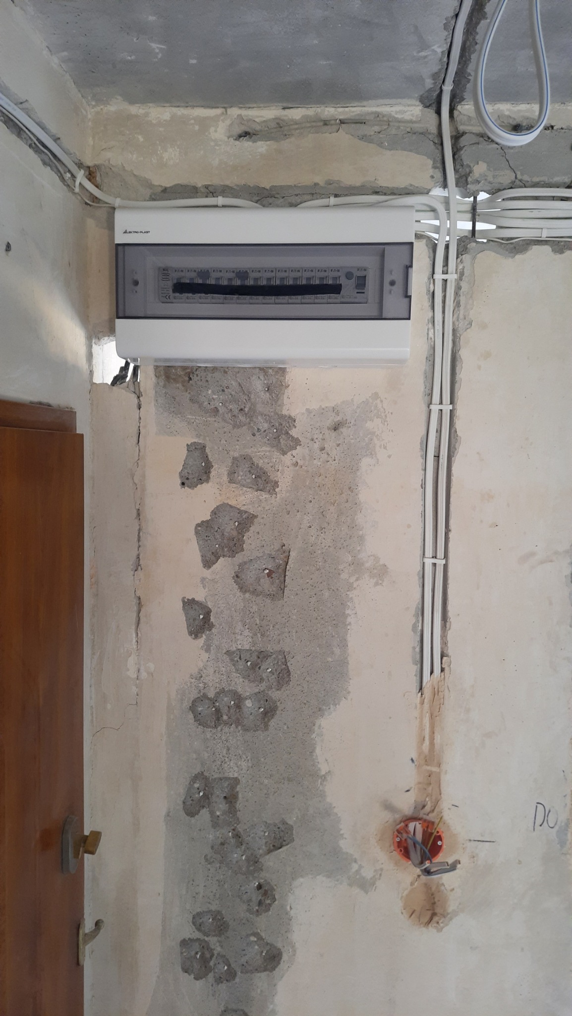 Nowa skrzynka rozdzielcza z widocznymi przewodami elektrycznymi zamontowana na surowej ścianie podczas remontu.