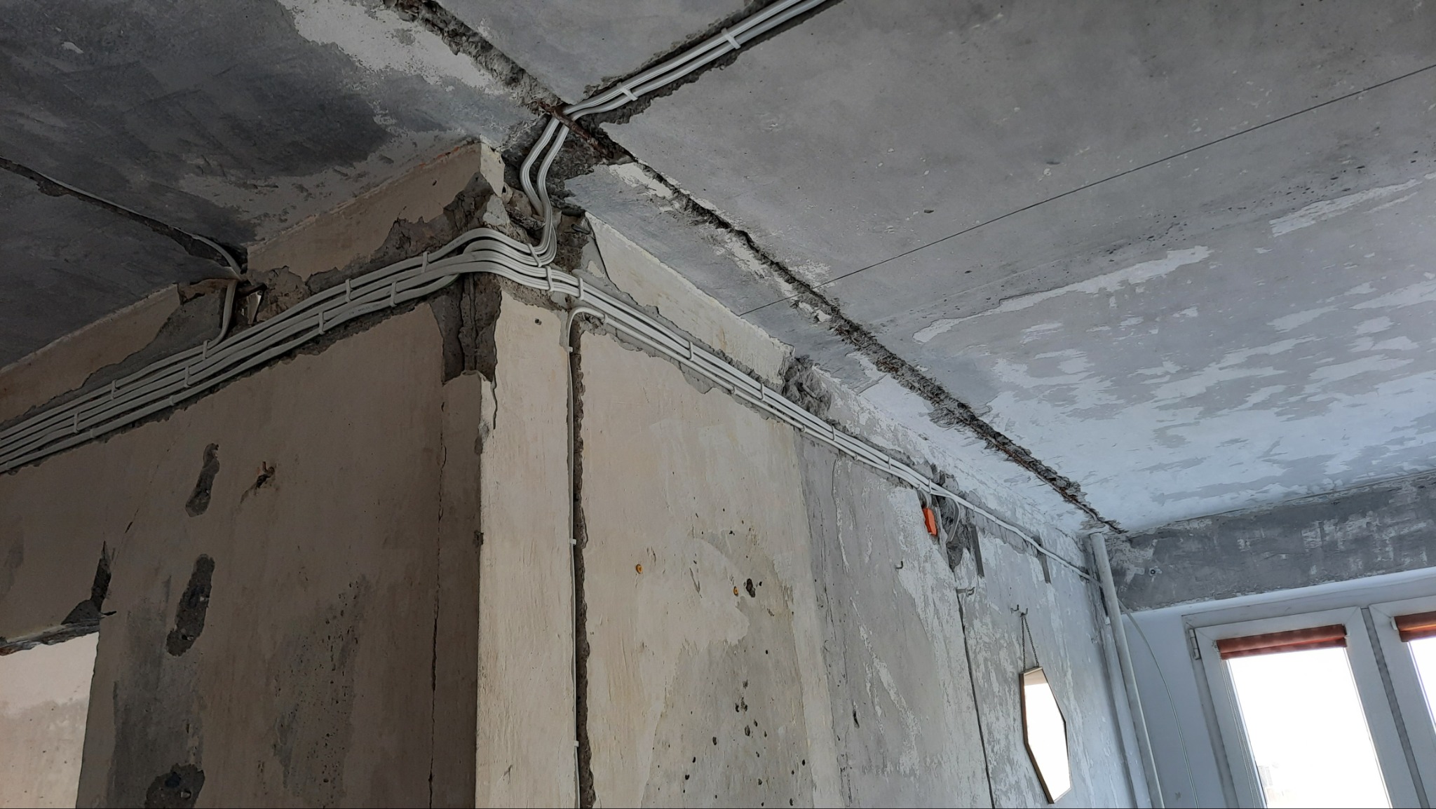 Białe przewody elektryczne ułożone wzdłuż surowych ścian i sufitu w trakcie remontu, widoczne fragmenty okna.