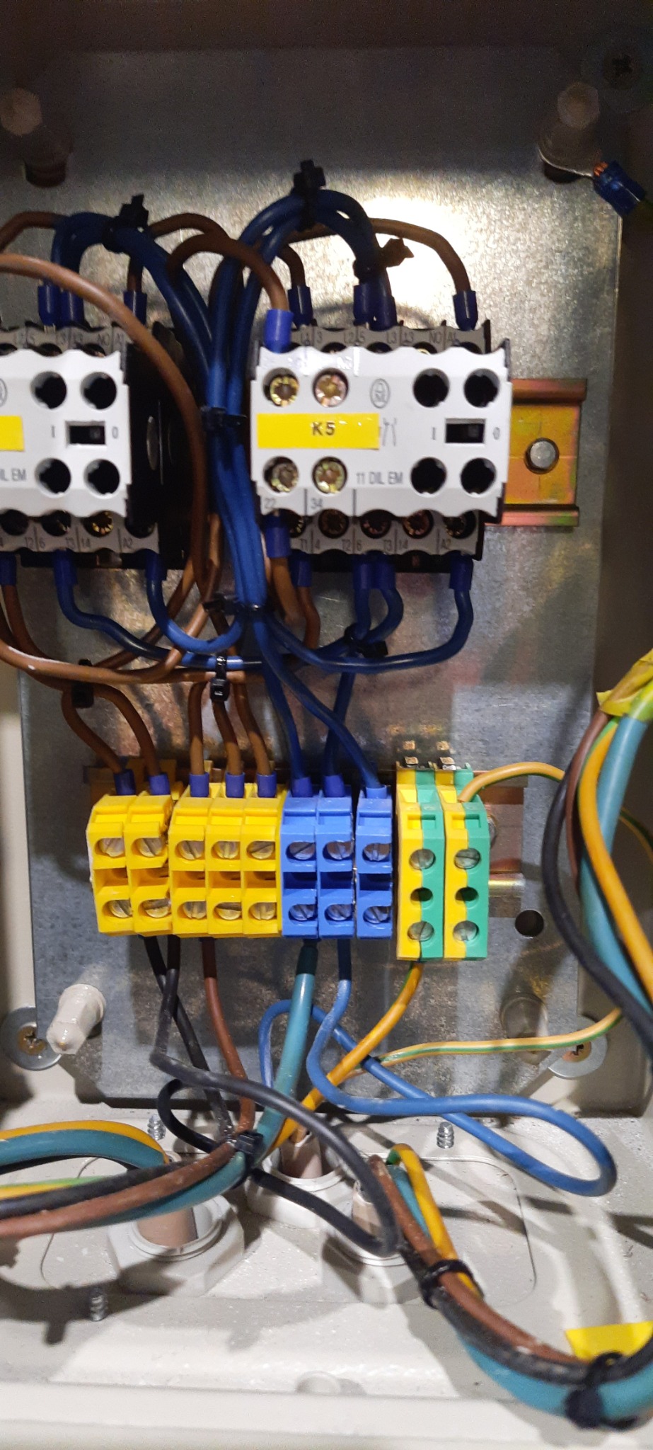 Wewnętrzny widok skrzynki elektrycznej we Włocławku, z widocznymi bezpiecznikami, złączkami w kolorach żółtym, niebieskim i zielonym oraz licznymi przewodami. Uwagę zwraca staranne ułożenie kabli.