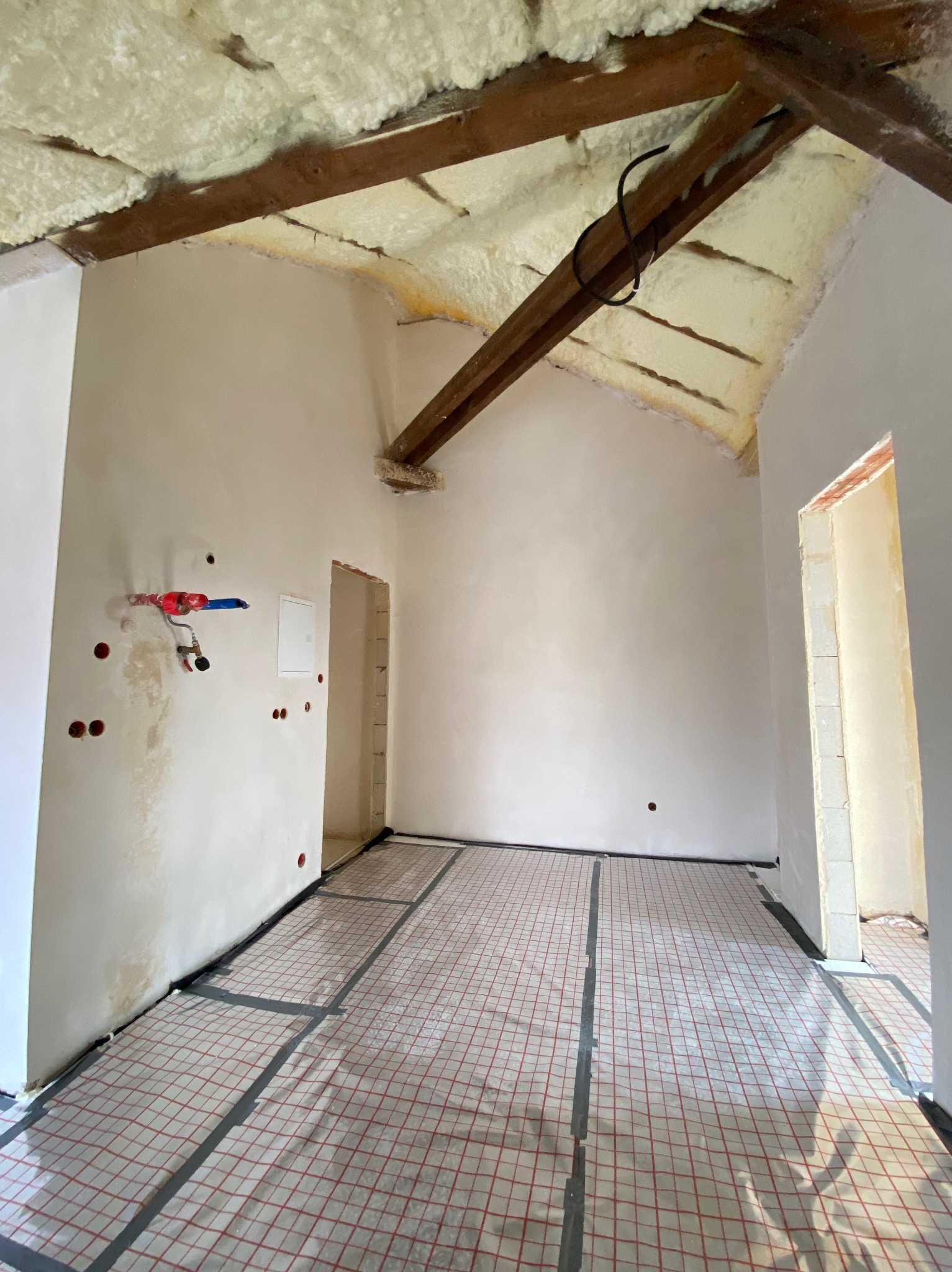 Poddasze po szpachlowaniu i izolacji pianą PUR, przygotowane do montażu ogrzewania podłogowego z widoczną siatką grzewczą i instalacją wodną na ścianie.