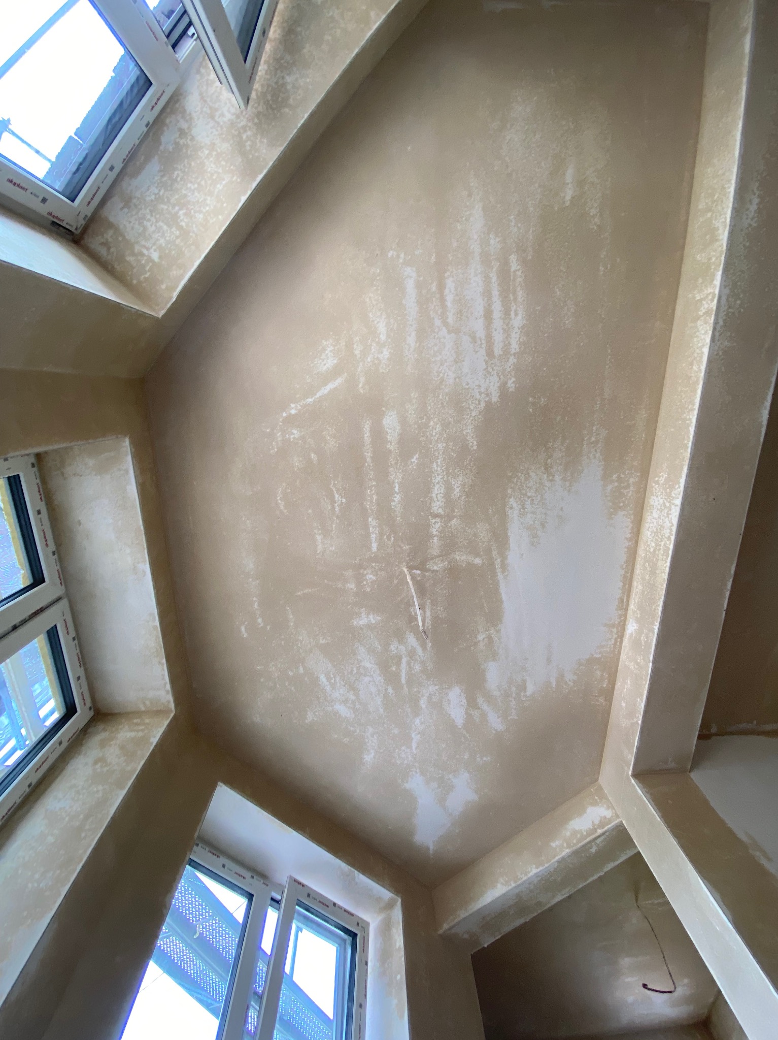 Sufit i ściany w trakcie prac przygotowawczych do malowania, widoczne ślady po szpachlowaniu, surowe oświetlenie, widok z dołu.