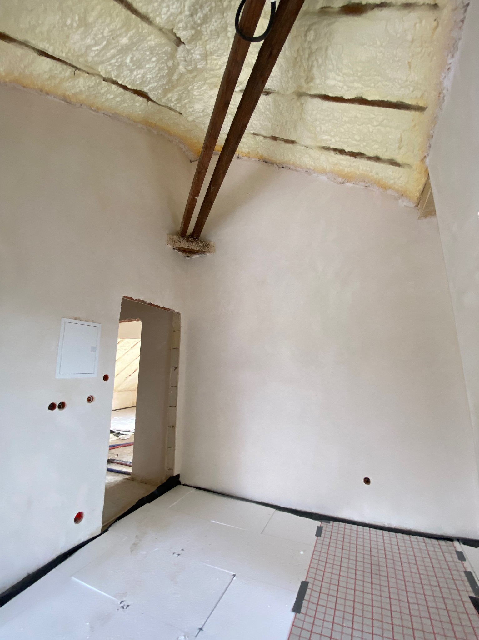 Poddasze w trakcie prac wykończeniowych: ocieplony strop z widocznymi belkami, ściany po nałożeniu pierwszej warstwy gładzi, przygotowane podłoże pod ogrzewanie podłogowe.