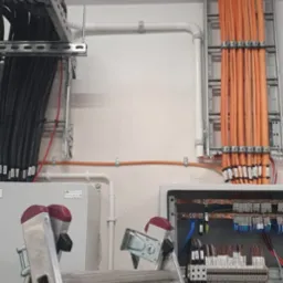 Rozdzielnia elektryczna z widocznymi kablami ułożonymi w korytkach i drabinkach kablowych, dostęp do rozdzielni zapewnia aluminiowa drabina Krause.