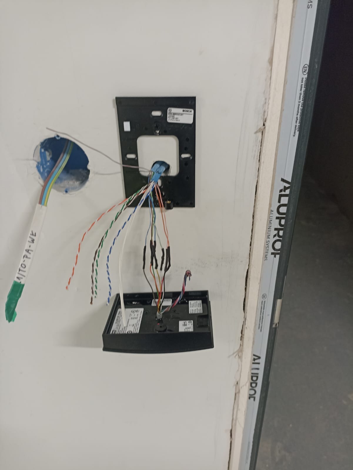 Montaż domofonu Bosch: widoczne przewody, puszka instalacyjna w ścianie i panel sterowania w trakcie podłączania, detale instalacji w surowym stanie.