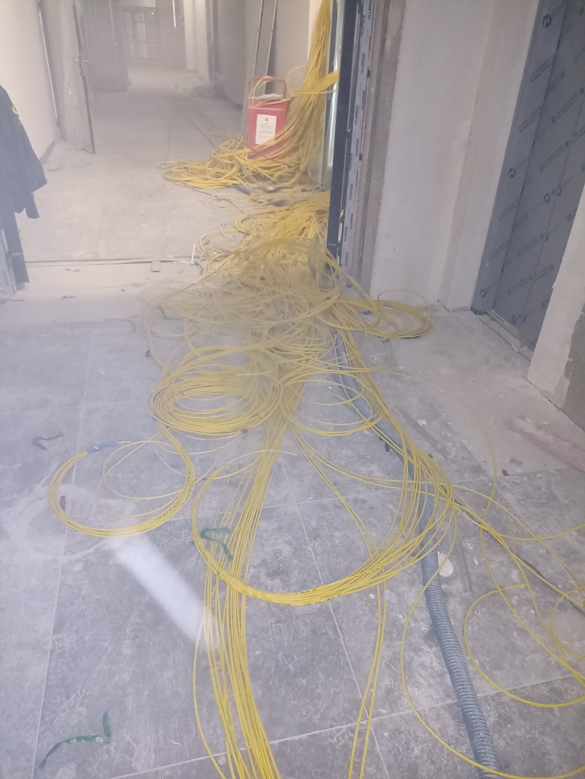 Rozciągnięte żółte kable elektryczne na podłodze w korytarzu w trakcie prac instalacyjnych w Brzezinach. Widoczny fragment ściany i drzwi.