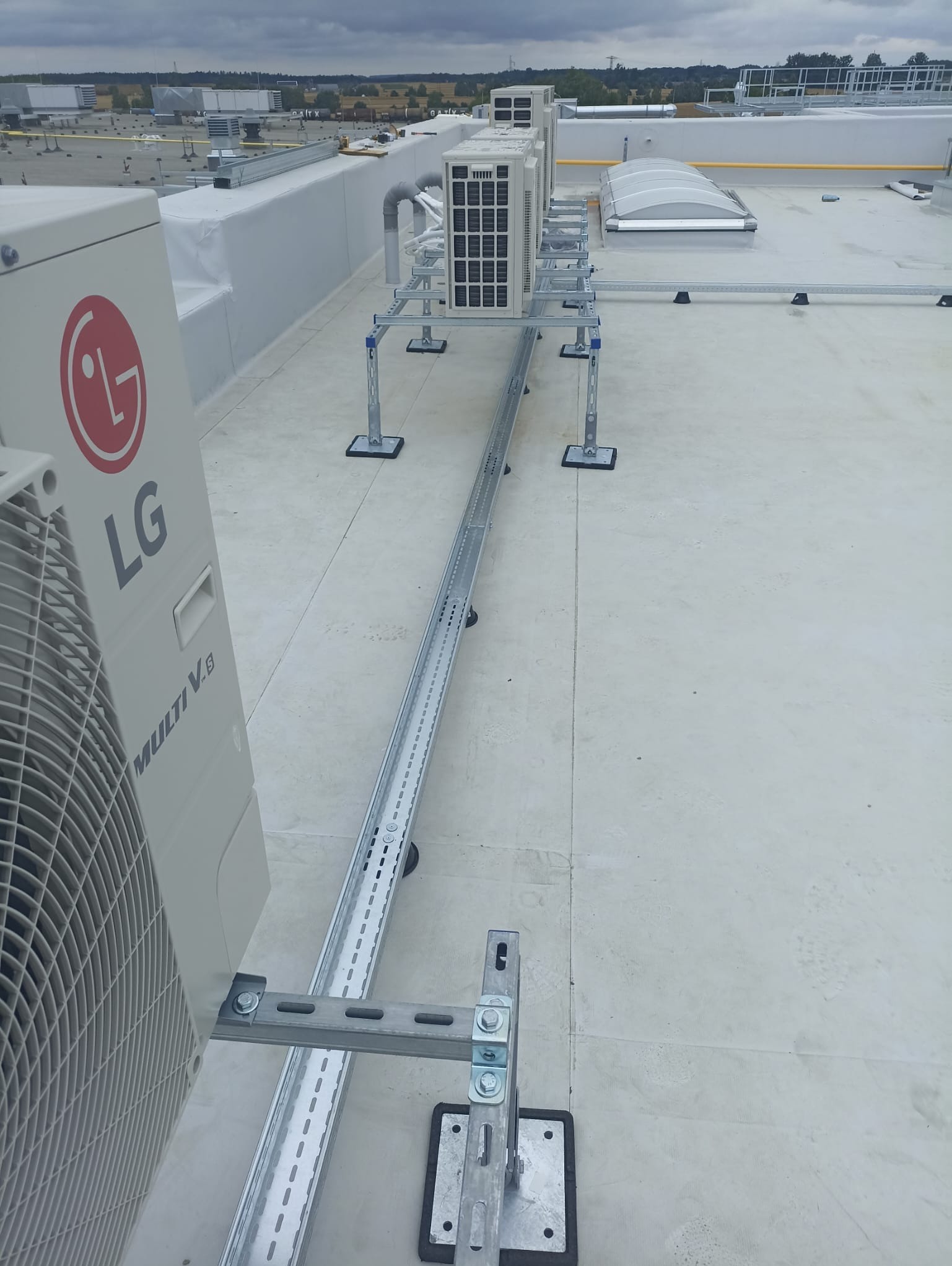 Instalacja klimatyzatorów LG Multi V na dachu budynku, widoczne wsporniki i korytka kablowe.