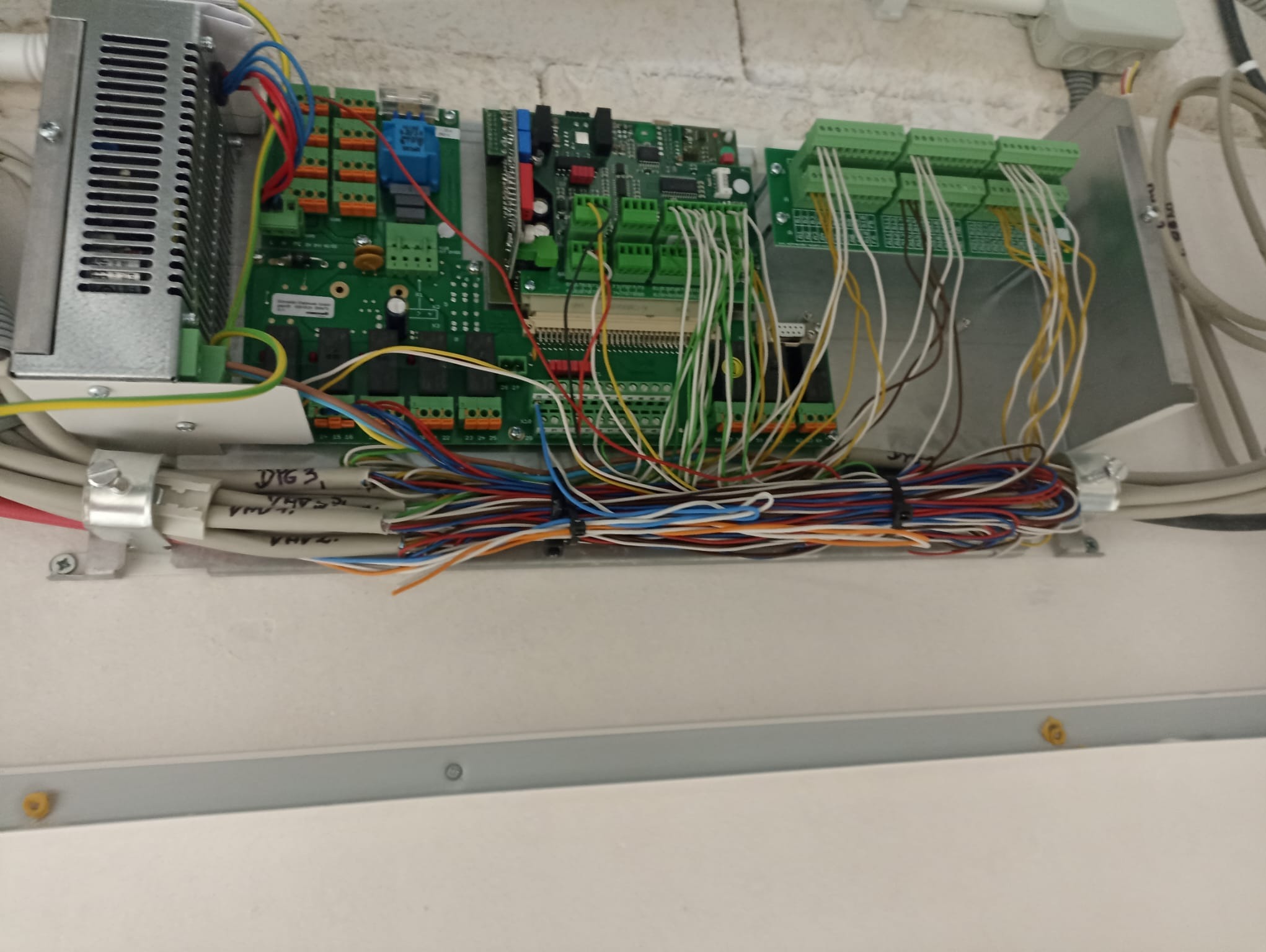 Rozdzielnica elektryczna z podłączonymi przewodami, widoczne złącza, moduły elektroniczne i zasilacz impulsowy, montaż wewnątrz obudowy.