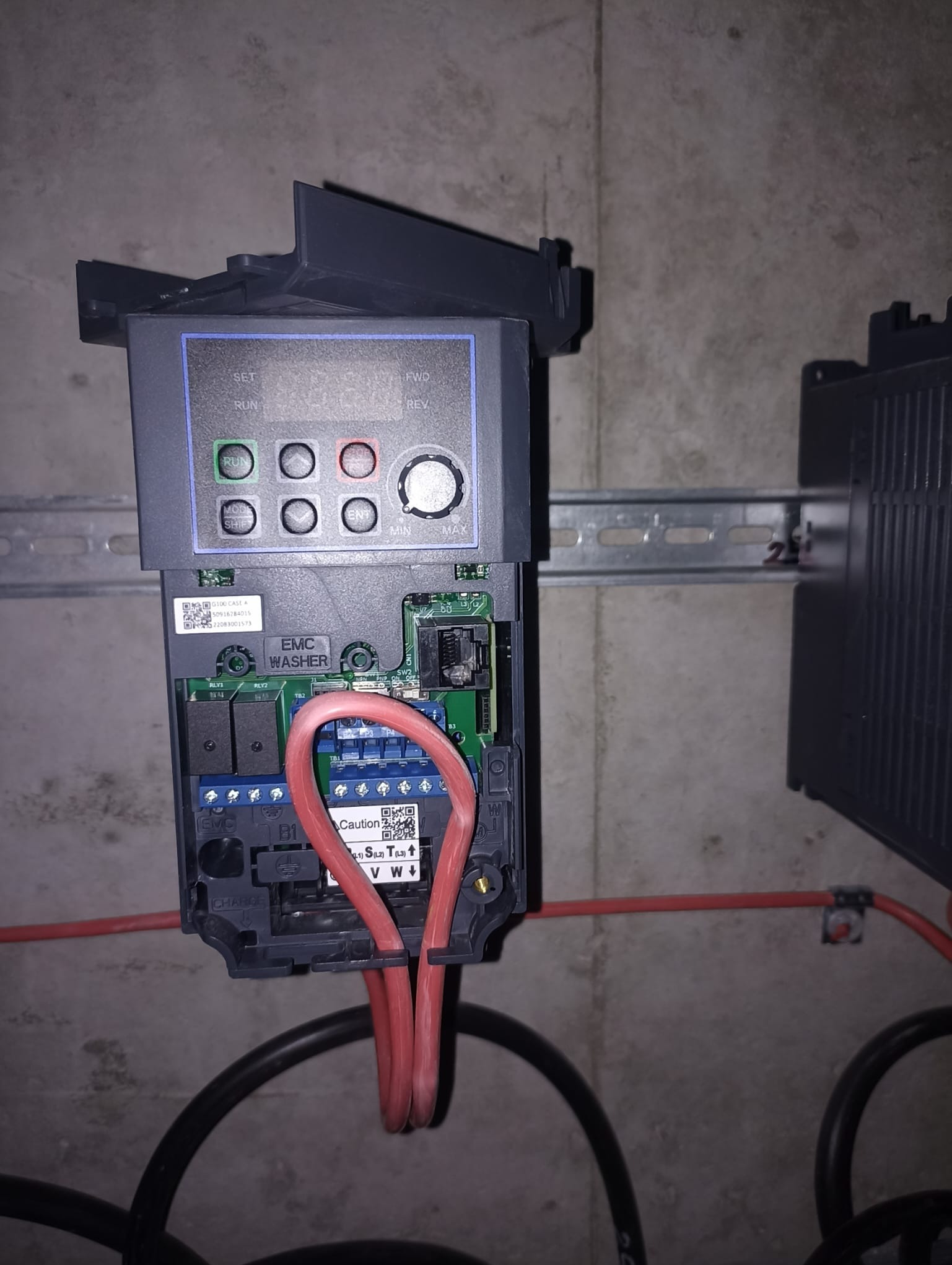 Panel sterowania automatyki przemysłowej z widocznymi przyłączami kablowymi, zamontowany na szynie DIN na tle szarej ściany.