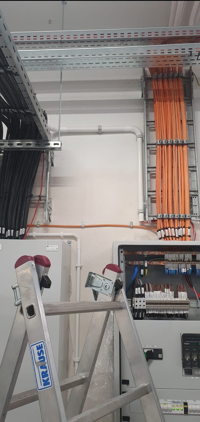Rozdzielnia elektryczna z widocznymi kablami ułożonymi w korytkach i drabinkach kablowych, dostęp do rozdzielni zapewnia aluminiowa drabina Krause.