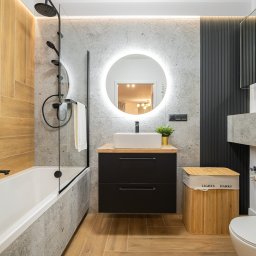 POD KLUCZ SPÓŁKA Z OGRANICZONĄ ODPOWIEDZIALNOŚCIĄ - Nowoczesna łazienka z drewnopodobnymi i szarymi płytkami, okrągłym lustrem z podświetleniem LED, czarną armaturą i drewnianym koszem na pranie z napisem 'LIGHTS DARKS'.