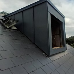 Wladyslaw Byczek - Nowa, grafitowa lukarna z metalowym obiciem na dachu pokrytym ciemną dachówką, widok z dołu na pochmurne niebo.