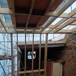 Wladyslaw Byczek - Wnętrze w trakcie remontu z odsłoniętą cegłą, widoczne drewniane rusztowanie sufitu i metalowe wzmocnienia, rusztowania na zewnątrz budynku.