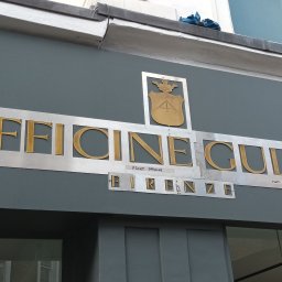 Wladyslaw Byczek - Szary budynek z metalowym szyldem 'Officine Gullo Firenze' z herbem, widoczne notatki i prowizoryczne mocowania.