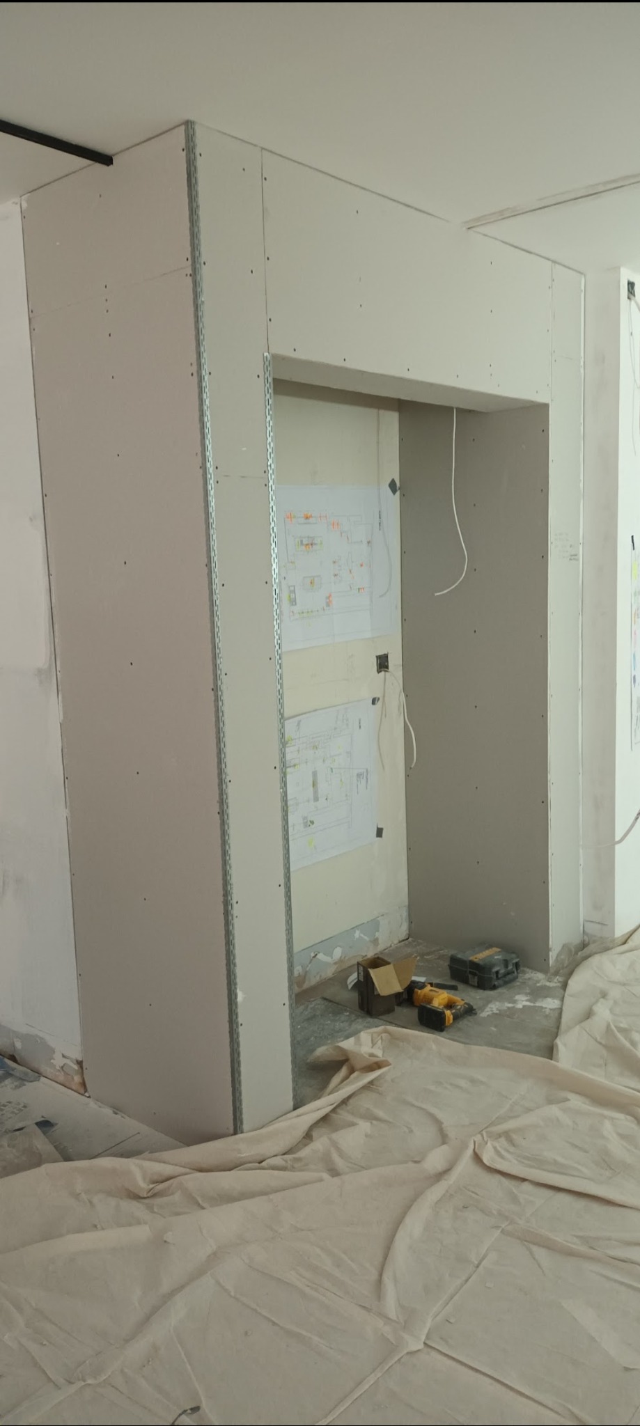 Montaż płyty karton gips w Tczewie: Widok na konstrukcję z profili i płyt GK tworzącą wnękę, z widocznymi narzędziami i planami na ścianie w tle, zabezpieczoną podłogą.