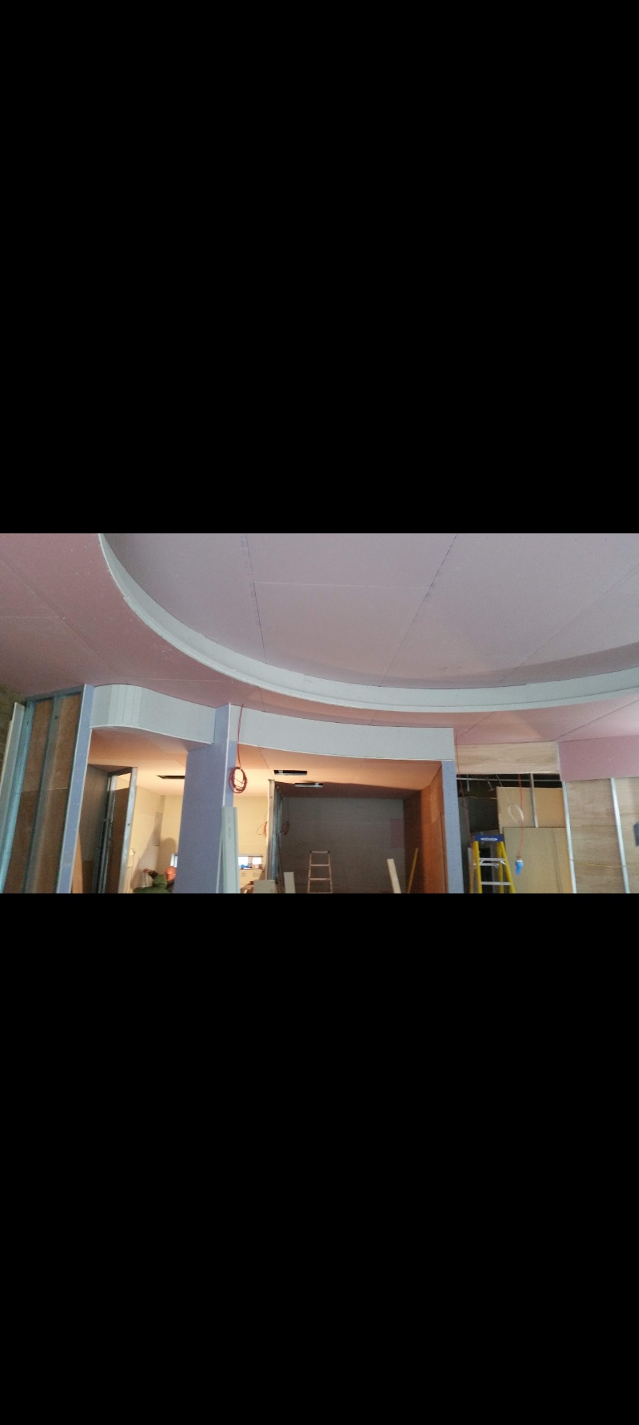 Sufit z płyt kartonowo-gipsowych z zaokrąglonymi elementami dekoracyjnymi w trakcie montażu, widoczne metalowe profile i drabina w tle.