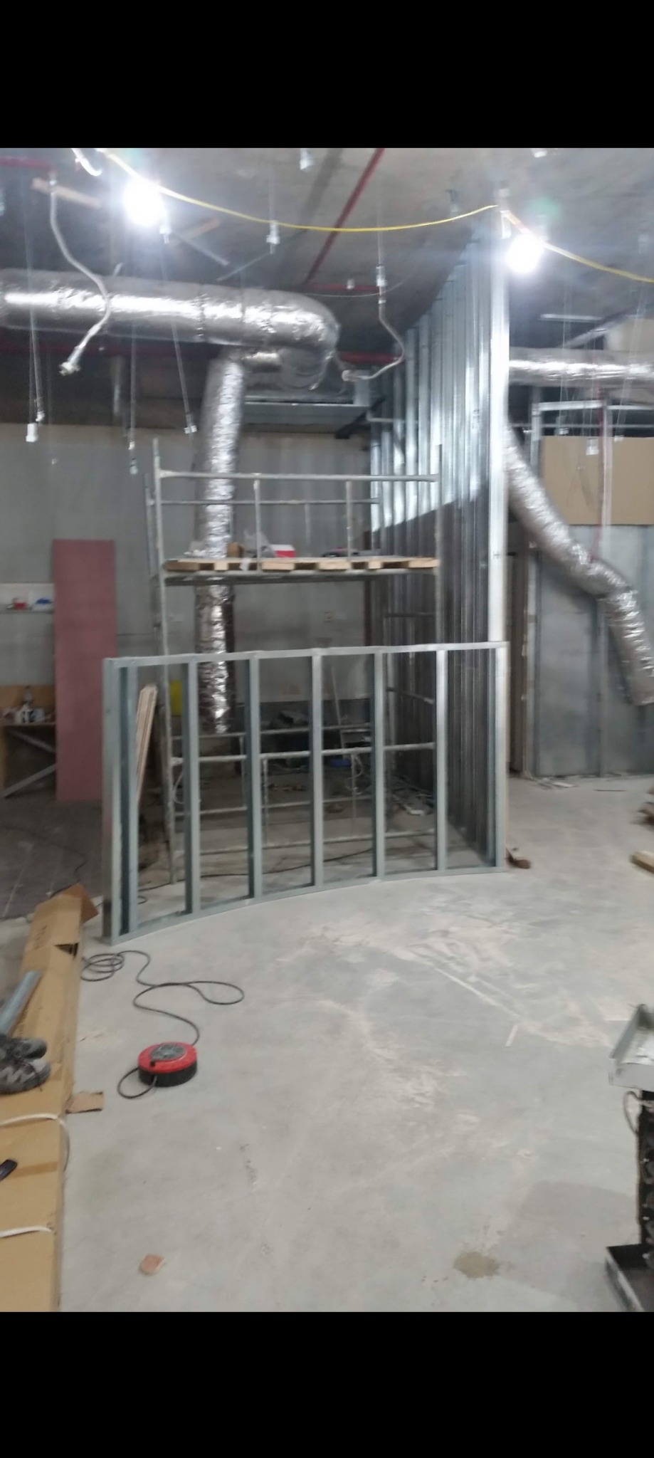 Metalowa konstrukcja ścian działowych w surowym stanie, widoczne przewody wentylacyjne pod sufitem, rozłożone narzędzia, etap budowy w pomieszczeniu komercyjnym.