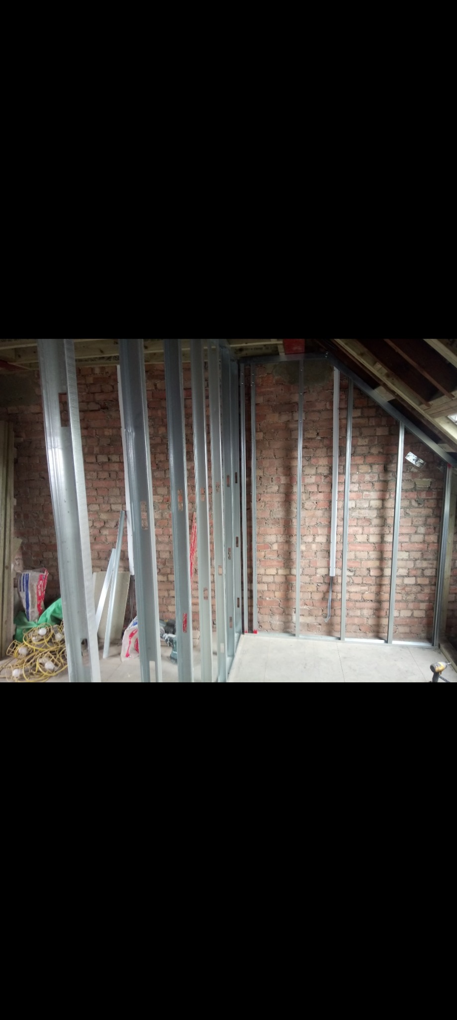 Montaż metalowej konstrukcji szkieletowej na ceglanej ścianie poddasza, widoczne profile pionowe i poziome, przygotowanie do obłożenia płytami.