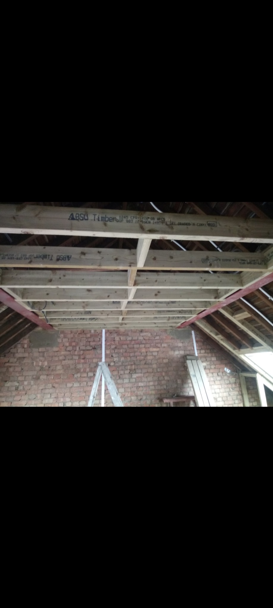 Montaż drewnianej konstrukcji sufitowej z widoczną ceglaną ścianą i podporą w trakcie prac wykończeniowych.