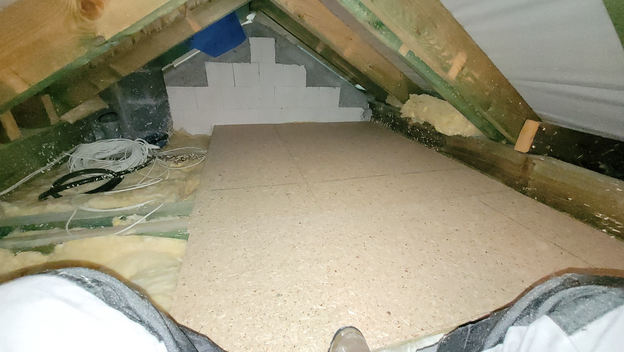 Adaptacja strychu: podłoga z płyt OSB ułożona na legarach, widoczne ocieplenie wełną mineralną i częściowo wymurowana ściana szczytowa z bloczków gazobetonowych.