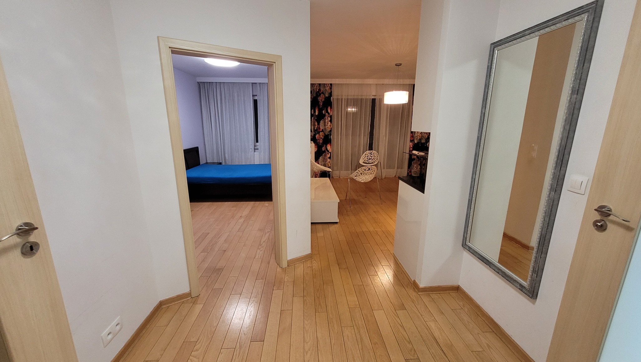 Ustawne mieszkanie po remoncie: widok z przedpokoju na sypialnię z niebieskim łóżkiem i salon z designerskimi krzesłami oraz drewnianą podłogą.