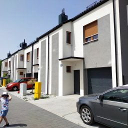 Budownictwo - Szereg nowoczesnych domów jednorodzinnych z garażami, pomalowanych w biało-szare pasy, z zaparkowanymi samochodami i dzieckiem na chodniku.