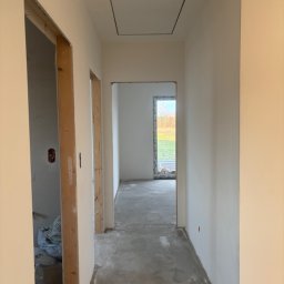 Dobra Robota Budowlana - Korytarz w trakcie prac wykończeniowych: surowe ściany, wnęki drzwiowe bez ościeżnic, betonowa podłoga. Widoczne przygotowania do dalszych prac.