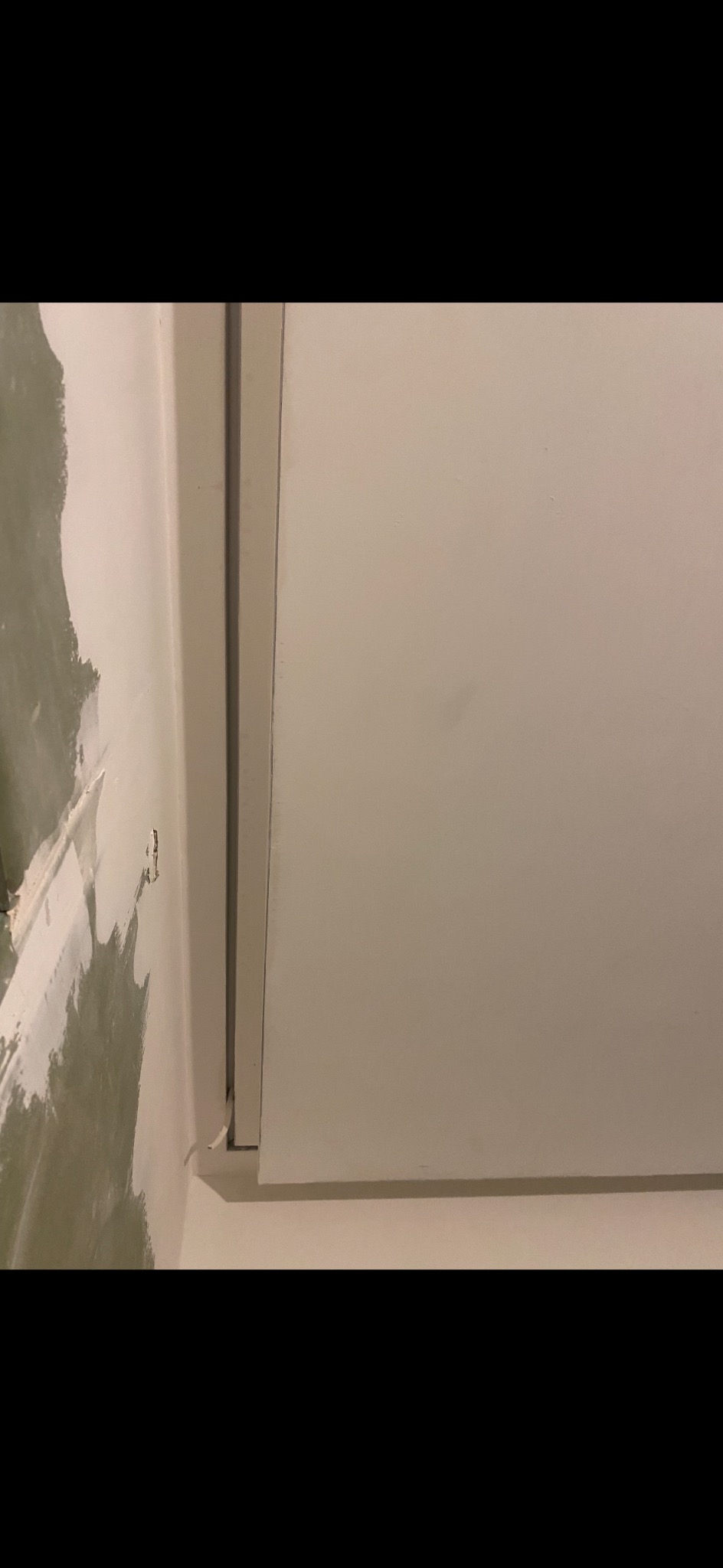 Fragment ściany po szpachlowaniu, widoczne nierówności i świeża warstwa gładzi. Przygotowanie do malowania, narożnik z listwą wykończeniową.