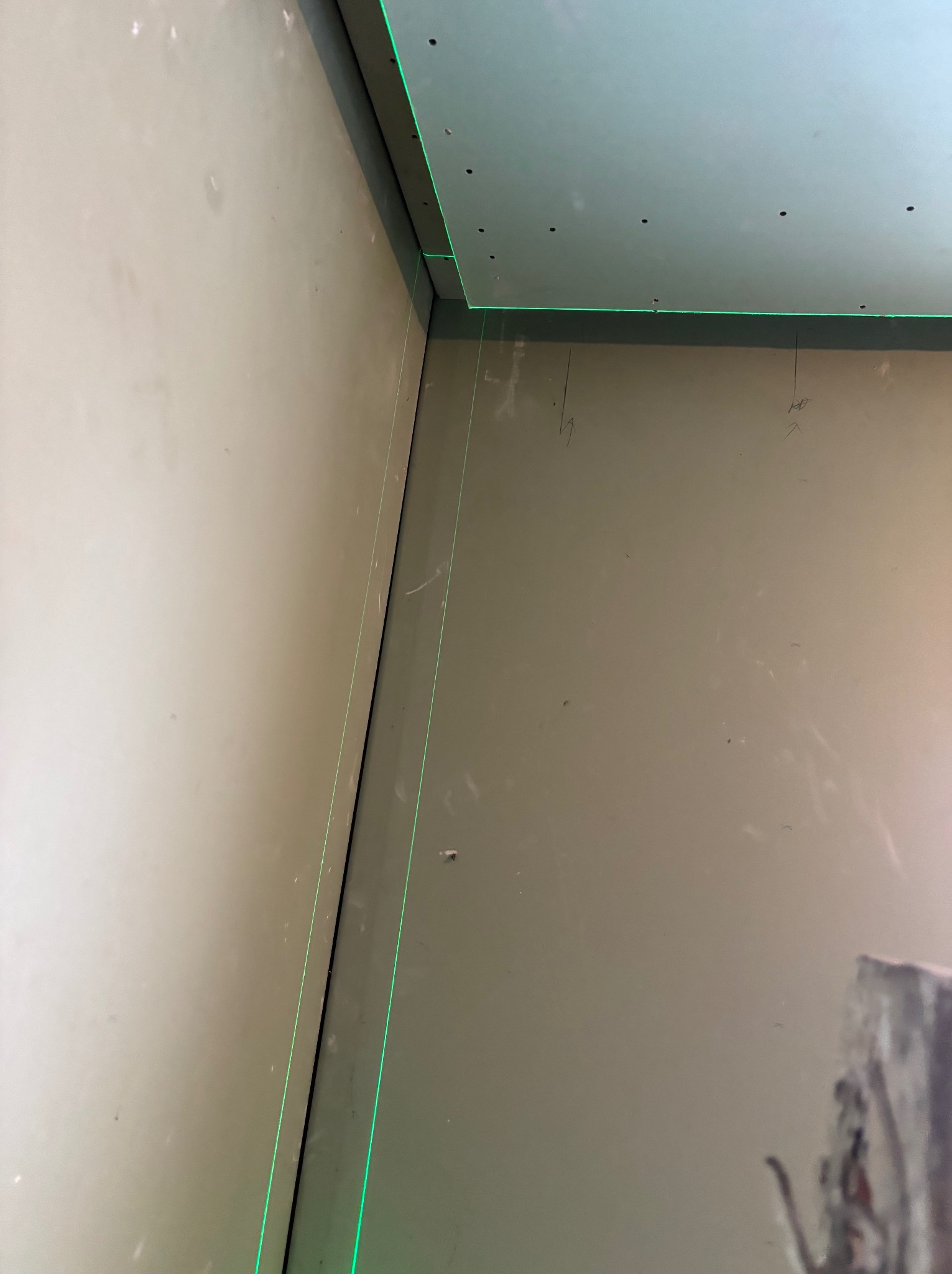 Ściana i sufit z płyt karton-gips, wyznaczony poziom laserem krzyżowym. Widoczne ślady po szpachlowaniu i otwory po wkrętach. Prace wykończeniowe w trakcie.