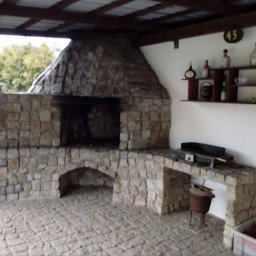 Marek - Kamienny grill ogrodowy z wędzarnią pod zadaszeniem, z blatem roboczym i półką na akcesoria, numer domu 43 na ścianie.