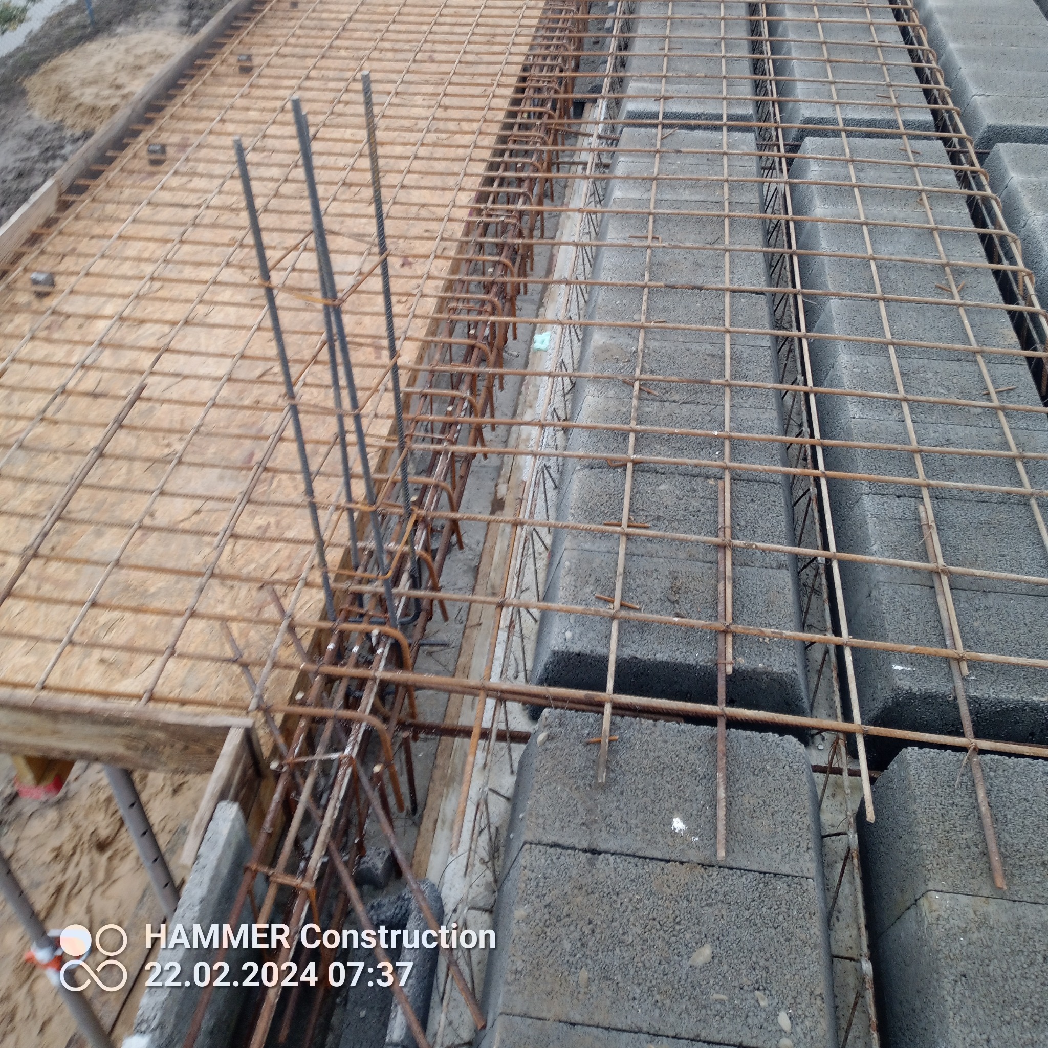 Zbrojenie i bloczki betonowe przygotowane do wylewki fundamentów, widoczne drewniane szalunki i wystające pręty zbrojeniowe.