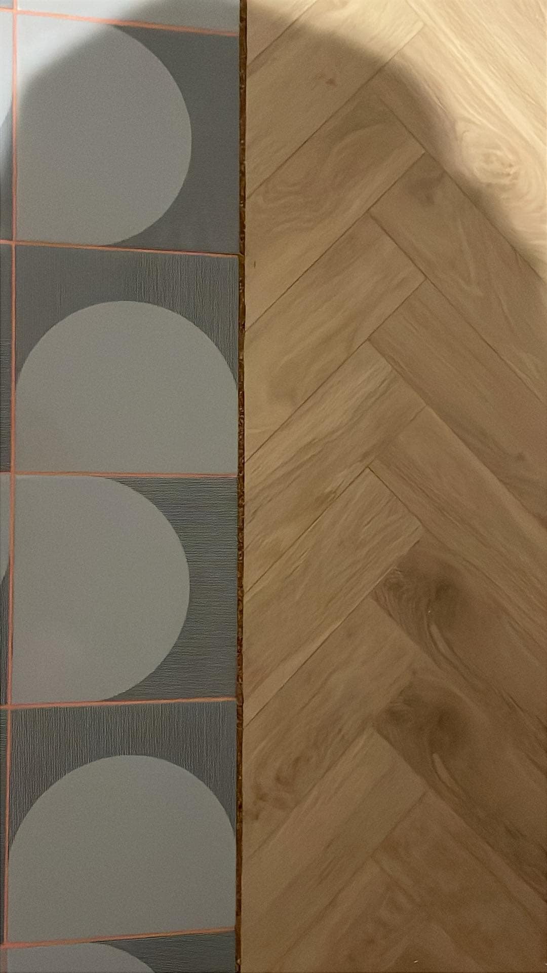 Połączenie płytek z motywem kół i parkietu ułożonego w jodełkę. Widoczny cień. Jasne drewno kontrastuje z szarością płytek.