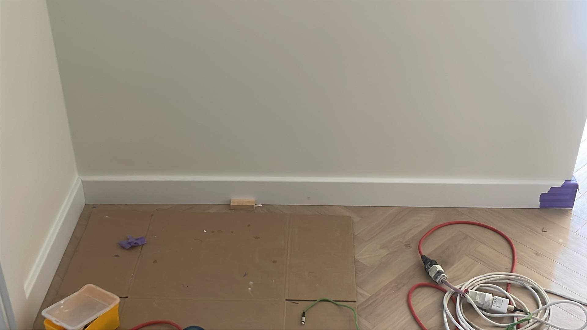 Montaż białych listew przypodłogowych w Krakowie. Ułożona podłoga w jodełkę, zabezpieczone narożniki taśmą malarską. Widoczne narzędzia pracy.