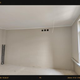Move- LINE - Jasne wnętrze po szpachlowaniu, przygotowane do malowania. Widoczne gładkie ściany, listwy sufitowe, otwory wentylacyjne i fragment instalacji w rogu pomieszczenia.