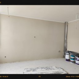 Move- LINE - Pokój w trakcie malowania: ściany w beżowym odcieniu, widoczne puszki z farbą, przygotowane do dalszych prac wykończeniowych. Minimalizm i stonowana kolorystyka.