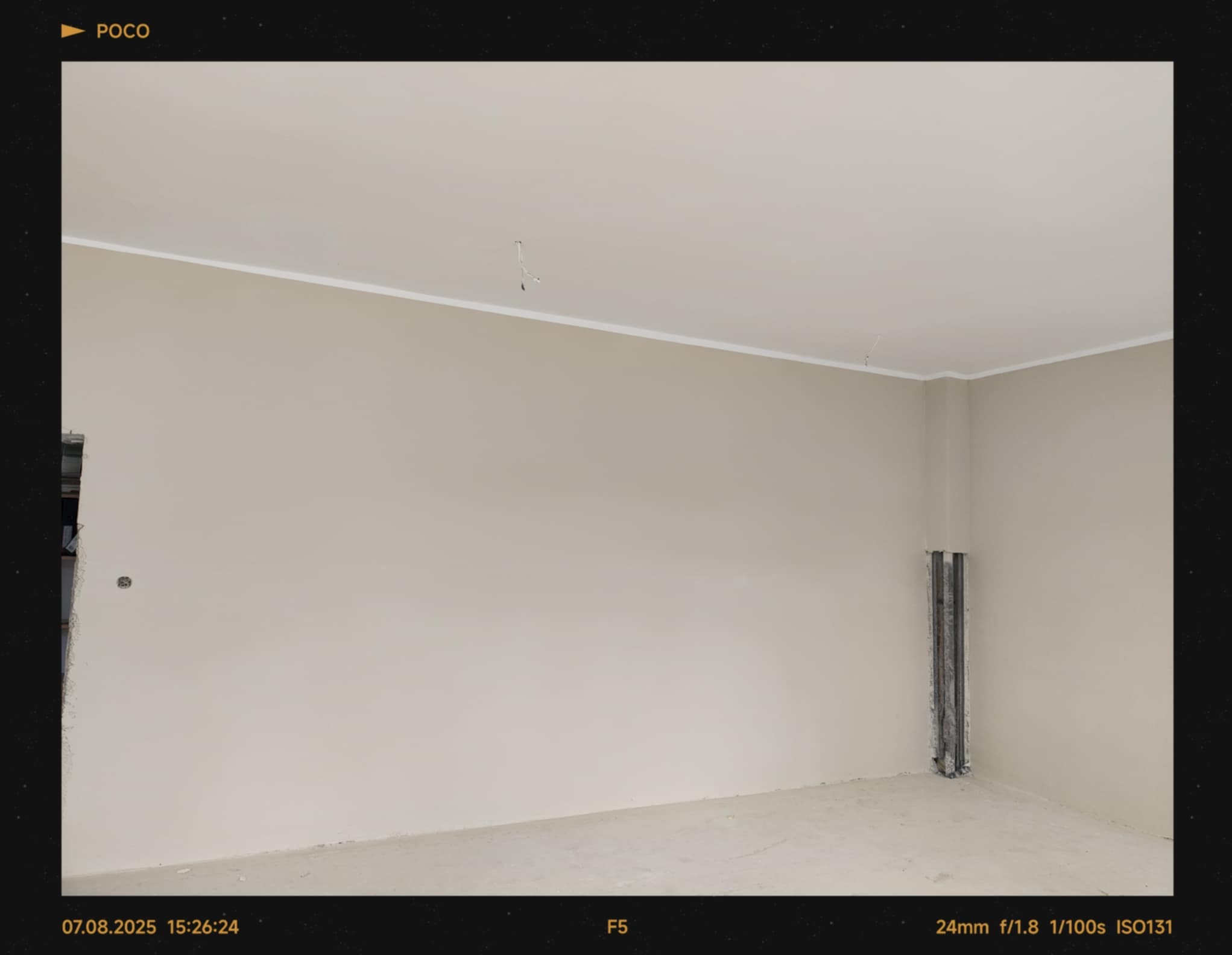 Jasny pokój po remoncie: świeżo pomalowane ściany w odcieniach beżu, białe listwy przysufitowe, widoczne piony instalacyjne. Minimalistyczny efekt wykończenia.