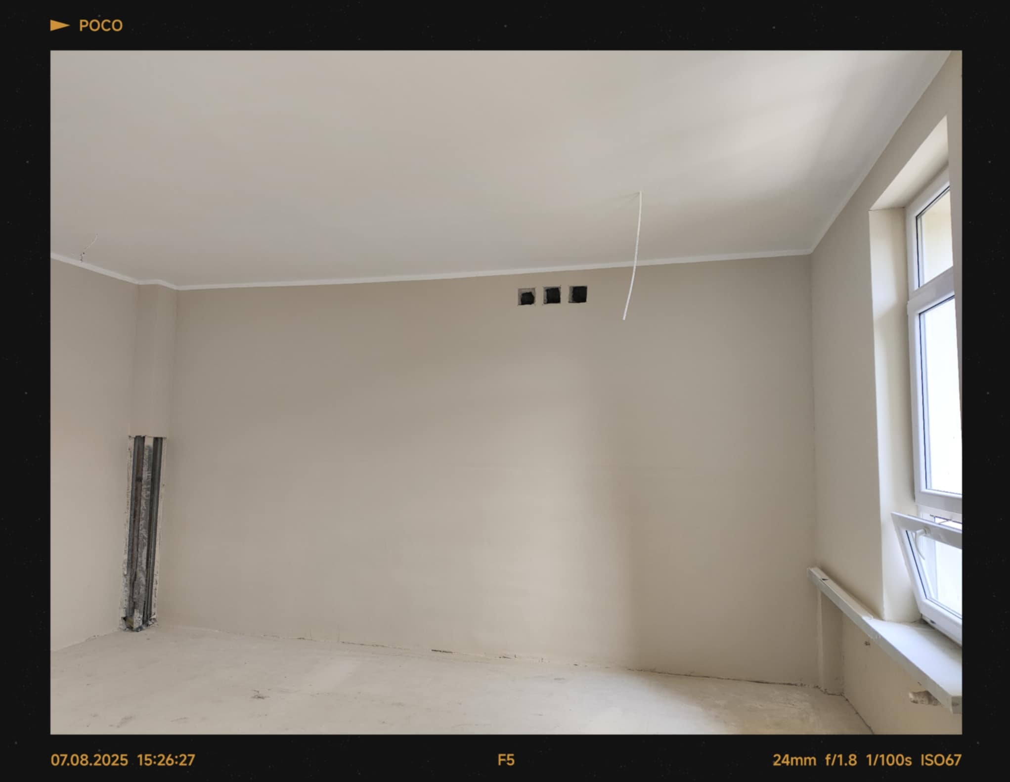 Jasne wnętrze po szpachlowaniu, przygotowane do malowania. Widoczne gładkie ściany, listwy sufitowe, otwory wentylacyjne i fragment instalacji w rogu pomieszczenia.