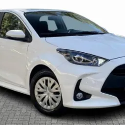 Biały samochód Toyota Yaris, widok z przodu na szarym brukowanym podłożu, z logo producenta na masce.