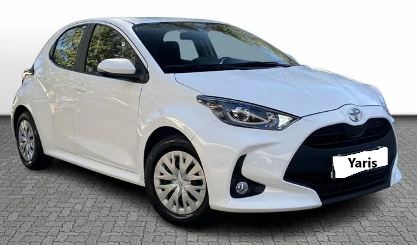 Biały samochód Toyota Yaris, widok z przodu na szarym brukowanym podłożu, z logo producenta na masce.