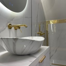 Welldonebathrooms.com - Elegancka łazienka: biała umywalka marmurkowa, złota armatura i mozaika. Podświetlane lustro dodaje blasku. Nowoczesny design z dbałością o detale.
